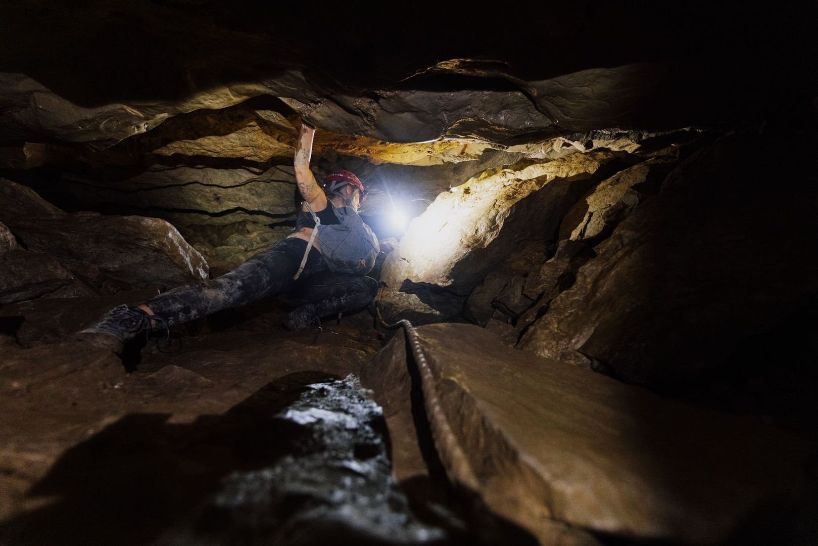 Spéléologue casqué progressant dans un étroit tunnel de lave sombre